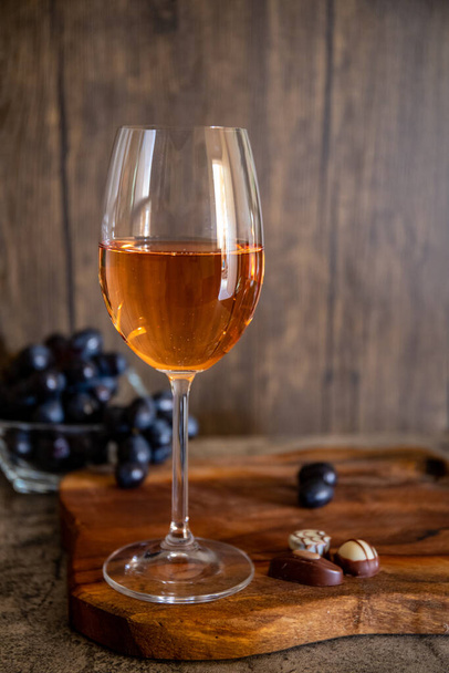 Rozenwijn in een glas op het houten bord met druiven op de achtergrond, verticaal formaat - Foto, afbeelding
