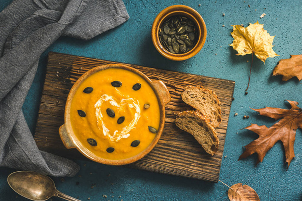 Ciotola con zuppa di zucca con panna e semi su una tavola di legno rustica su sfondo blu, vista dall'alto - Foto, immagini