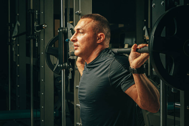 Fit man doing squats in a training machine - Фото, изображение