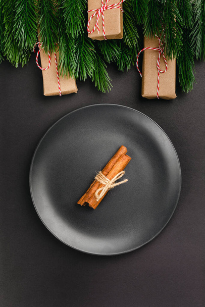 Christmas invitation card for Christmas dinner, bunch of cinnamon on black plate on black table with Christmas decor - Foto, Imagem
