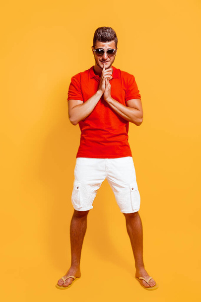 Full length of hipster man in red t-shirt and white shorts in sunglasses stands on yellow background - Фото, зображення