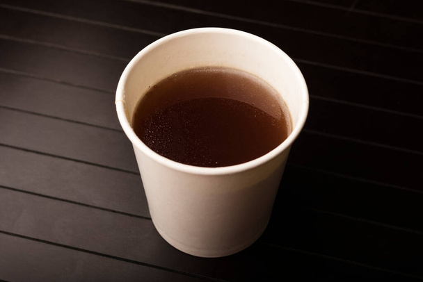 paper glass with delicious beef broth, dark background. Disposable tableware concept - Fotó, kép