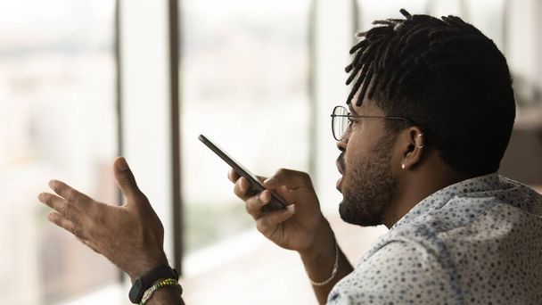 Young multiracial man recording audio message on cellphone. - Zdjęcie, obraz