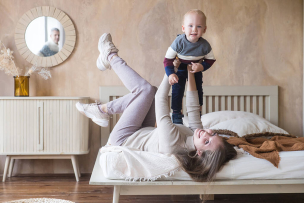 Vidám fiatal anya hold fia kisgyermek utánozni sík repülni szórakozás játék vicces játék feküdt az ágyon kényelmes otthon - Fotó, kép
