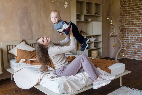 Joyful young mother hold son toddler imitate plane fly having fun play in funny game lying on bed in cozy home - Fotografie, Obrázek