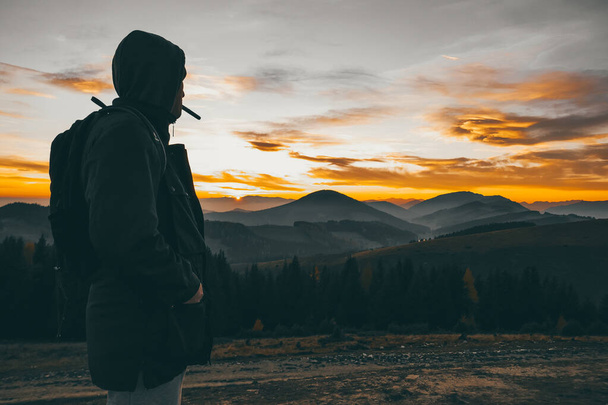 The guy stands and smokes in nature. Sunset in the mountains and tourists. - 写真・画像