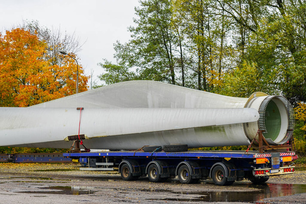 Una vista de un camión, un semirremolque de carga baja con piezas de turbina eólica de gran tamaño en el estacionamiento en el día de otoño - Foto, imagen