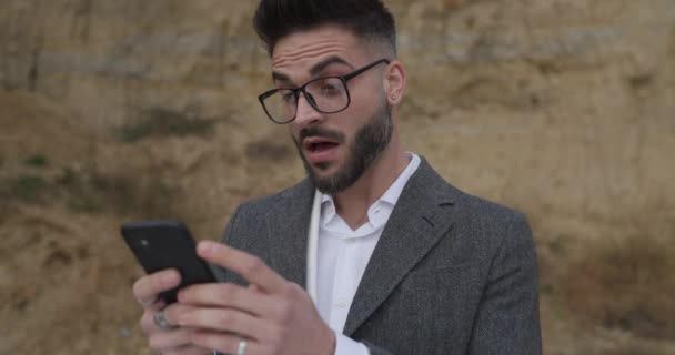 surprised sexy bearded man holding telephone, reading messages, making shocked face, smiling and making ok gesture outside in nature - Filmmaterial, Video