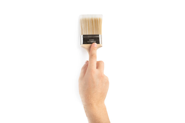Un pincel en la mano de un hombre. Concepto de renovación. Suministros y herramientas para pintar paredes aisladas en blanco - Foto, Imagen