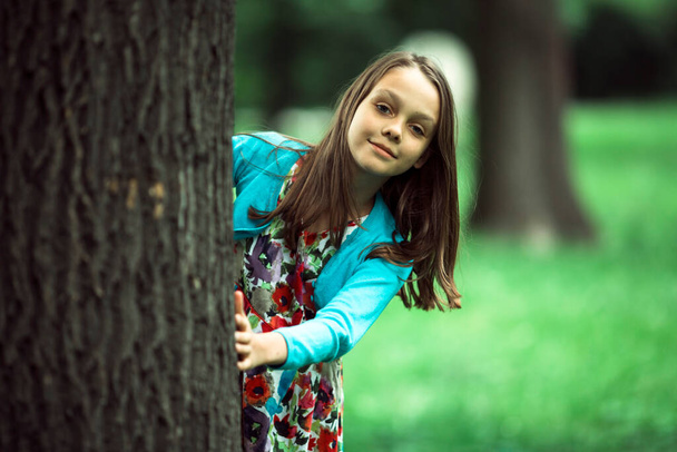 A girl looks out from behind a tree in the park. - Fotografie, Obrázek