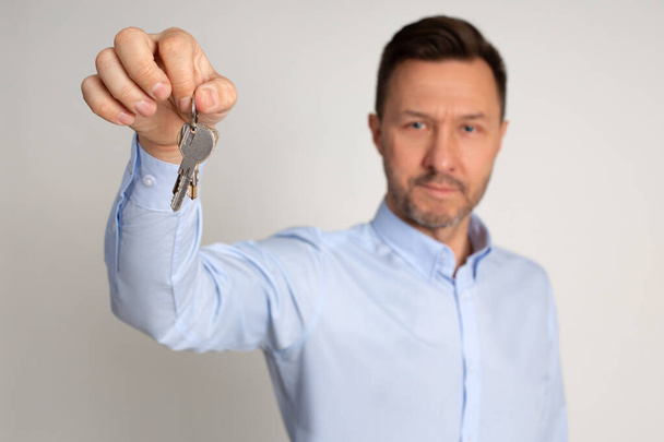 Photo of employee manager in shirt of real estate agency holds in hands keys to appartments. Buying or renting house. man is happy to become home owner. Studio shot on neutral background.  - Photo, image