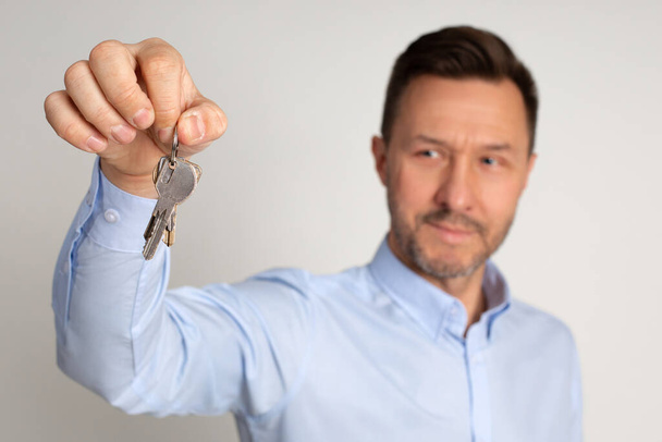 Photo of employee manager of real estate agency holds in hands keys to appartments. Buying or renting house. man is happy to become home owner. Studio shot on neutral background - Photo, image