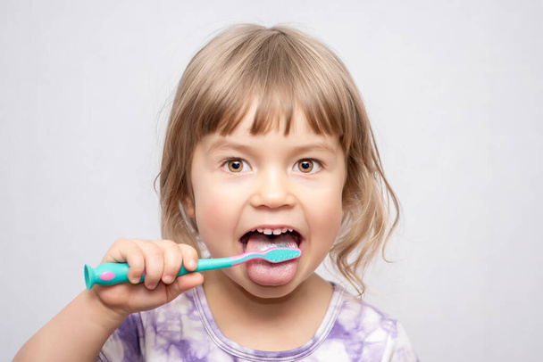 A little girl cleans her tongue and teeth with a toothbrush. Oral hygiene. - Φωτογραφία, εικόνα