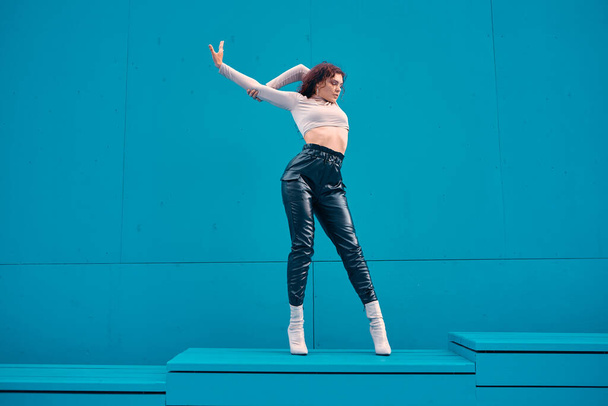 Stylish young sexy fit girl female model posing outdoors by blue wall with copy space for ad. Woman urban lifestyle - 写真・画像