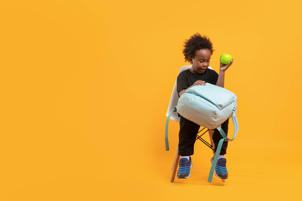 Black child boy 3 years, Students kid with school bag sitting complain own while hold a green apple, Isolated portrait on yellow background with copy space - Fotoğraf, Görsel