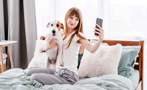Mädchen mit Hund und Smartphone im Bett - Foto, Bild