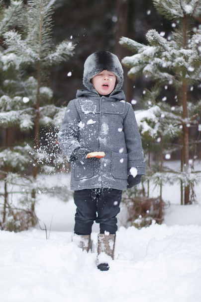 コートを着た男の子と帽子は、バゲルを食べながら雪玉に打たれます. - 写真・画像