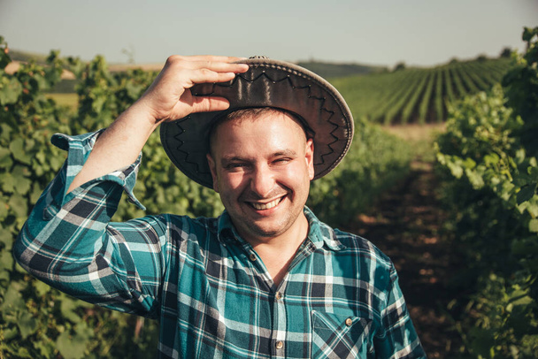 cheerful man with modern young winemaker hat is on the vineyard. - Φωτογραφία, εικόνα