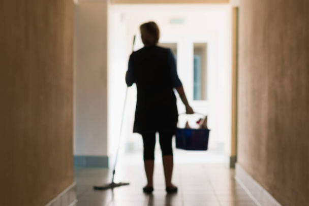Egy elmosódott kép egy nőről, aki takarítja a helyiségeket a folyosó és az iroda takarítása közben. - Fotó, kép