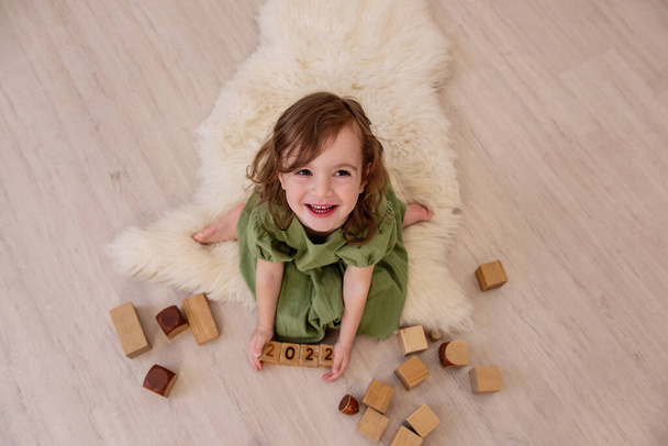 Top view of girl who holds wooden cubes with the numbers 2022 in her hands. The child plays in the construction of the tower. Active home games. Lifestyle kids education concept. Copy space, close up - Fotó, kép