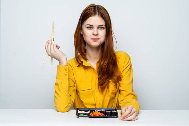 a woman in a yellow shirt sits at a table and eats sushi - Zdjęcie, obraz