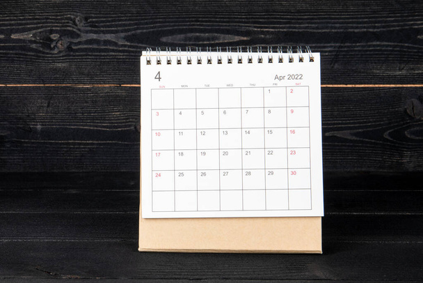April 2022. Kalender en planner op een zwarte houttextuur achtergrond - Foto, afbeelding