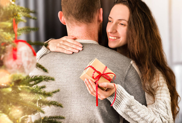 gelukkig jong vrouw knuffels man en houdt geschenk doos in de hand - Foto, afbeelding