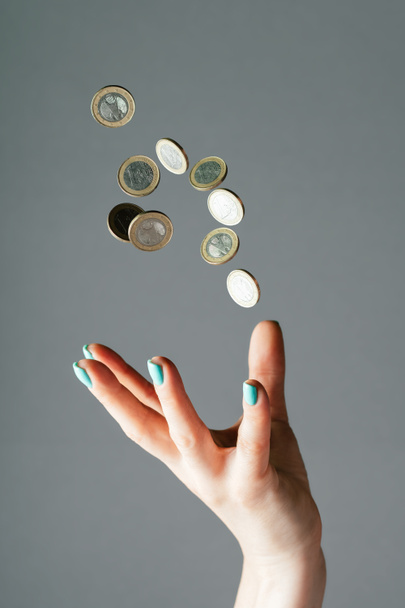 Female hand with blue nails throwing money, one euro coins into air on gray background. Levitating cash. Copy space, vertical - Foto, Imagen