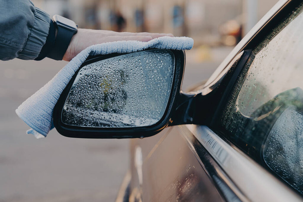 Hand van de mens wassen auto kant achteruitkijkspiegel met microvezel doek doek, vegen waterdruppels - Foto, afbeelding