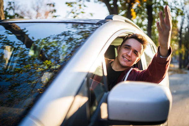 Blisko na jeden młody biały mężczyzna jazdy samochodem sam w słoneczny jesienny dzień patrząc na boku skopiować przestrzeń prawdziwych ludzi pochylając koryta okna machając i uśmiech szczęśliwy - Zdjęcie, obraz