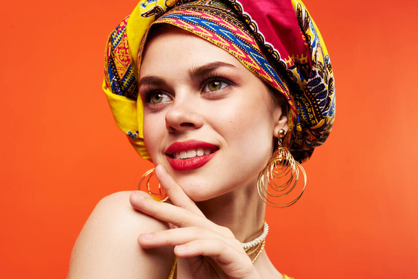 красивая женщина в разноцветной тюрбан привлекательный вид ювелирные изделия красный фон - Фото, изображение