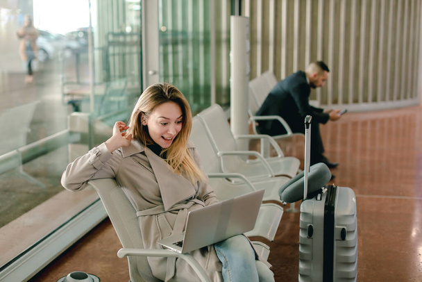 Kaukaski dziewczyny, siedząc w poczekalni z laptopa w pobliżu walizka. - Zdjęcie, obraz