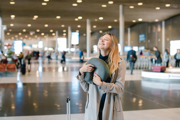 Mujer de pie en la sala del aeropuerto con valise y almohada para el cuello
. - Foto, Imagen