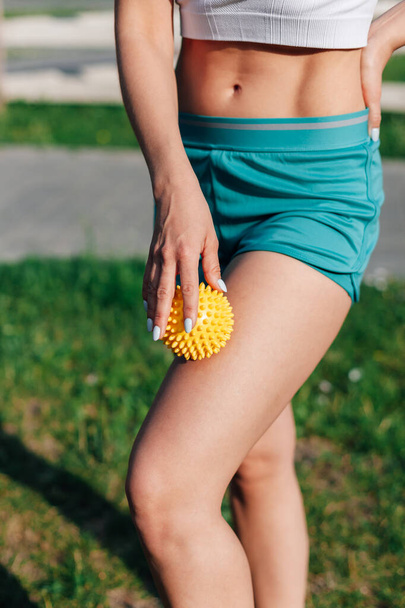 spiky rubber massage ball in hands of young woman in shorts for cellulite reduction and weight loss on lawn in garden on summer morning - Φωτογραφία, εικόνα