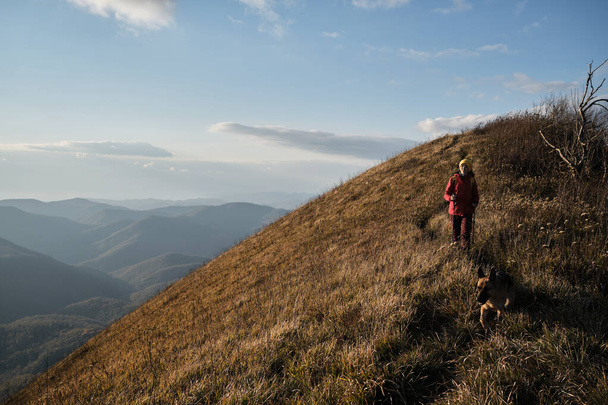 Γυναίκα ταξιδιώτης περπατά κατά μήκος στενό μονοπάτι στην κορυφή του βουνού με το σκυλί της. Διαδρομή πεζοπορίας στο εθνικό πάρκο. Γερμανικός Ποιμενικός ταξιδεύει με ιδιοκτήτη. - Φωτογραφία, εικόνα