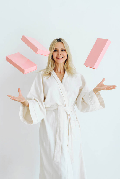 A European blonde in a robe throws pink boxes. White backgroun - Photo, Image