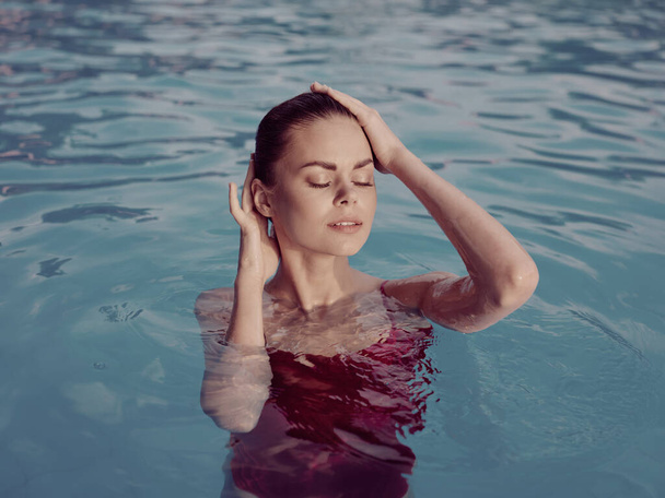 vrouw in rood badpak houden haar hoofd zwembad natuur luxe - Foto, afbeelding