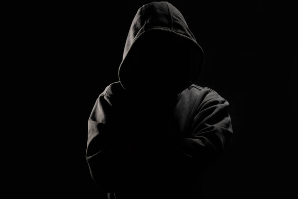 Mann ohne Gesicht mit Kapuze auf dunklem Hintergrund. - Foto, Bild