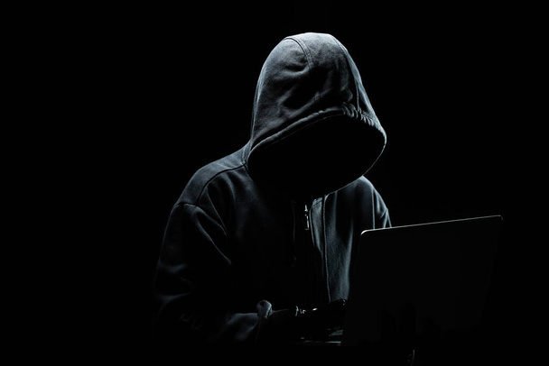 Хакер без обличчя в капоті з ноутбуком в темряві
. - Фото, зображення