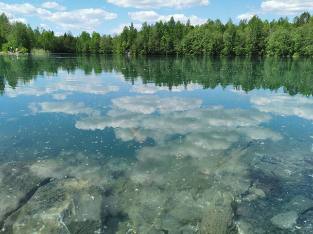 The shore of the lake is bright with clear water, in which you can see the marble on the bottom and reflect the sky with clouds, in the mountain park Ruskeala. - Photo, Image