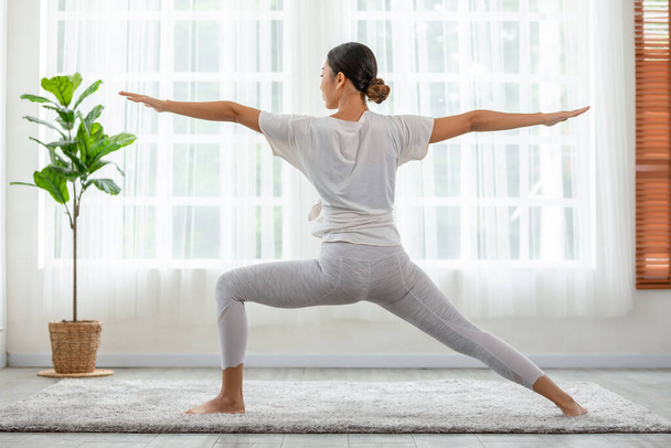 Calm of wellness Asian young woman standing breathing with yoga Warrior two pose,Yoga meditation of young healthy woman relax and comfortable at white cozy home,Yoga Exercise for Wellness Concept - 写真・画像