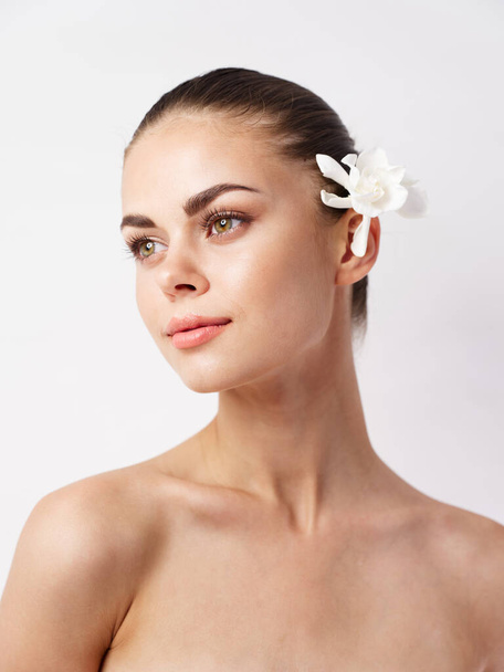 beautiful woman with bare shoulders bright makeup white flower look to the side - Photo, Image