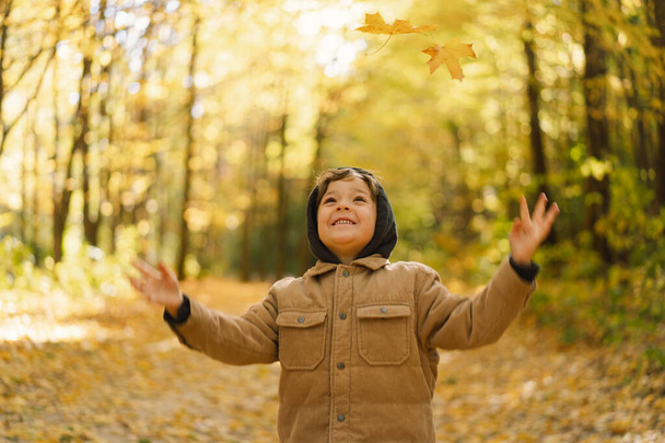 Niño pequeño y feliz niño riendo y jugando en el día de otoño. Niño jugar con hojas - Foto, imagen