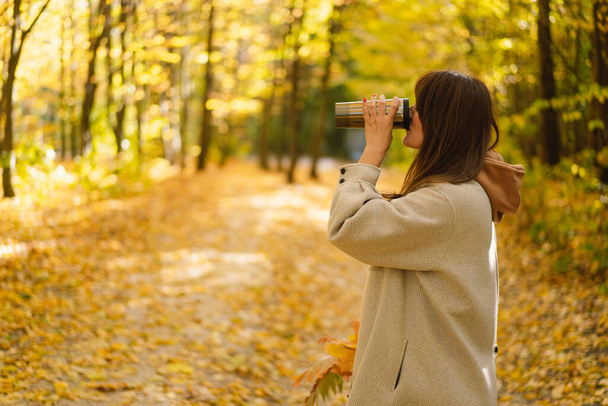 Молода жінка в довгій сорочці з термокухою в руках проходить через осінній ліс
. - Фото, зображення