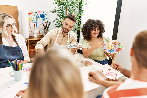 Ομάδα ανθρώπων χαμογελώντας χαρούμενη ζωγραφική κάθεται στο τραπέζι στο στούντιο τέχνης. - Φωτογραφία, εικόνα