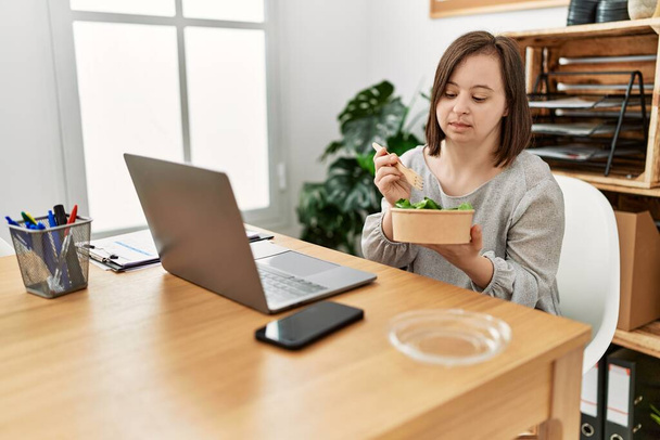 Bruna donna con sindrome di Down che lavora mangiando insalata in ufficio - Foto, immagini