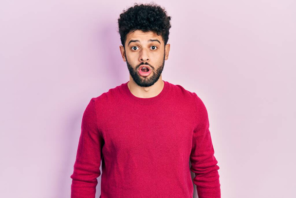 Jeune homme arabe barbe vêtu d'un pull rose décontracté effrayé et étonné avec la bouche ouverte pour la surprise, visage incrédule  - Photo, image