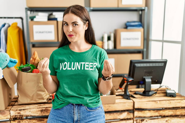 Nuori brunette nainen yllään vapaaehtoinen t paita lahjoituksia seistä tekee rahaa ele käsin, pyytää palkkaa, miljonääri liiketoimintaa  - Valokuva, kuva
