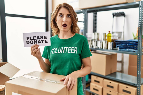 Gönüllü tişört giyen orta yaşlı bir kadın lütfen pankart bağışlasın. Korkmuş ve ağzı açık bir şekilde şaşkınlık içinde, inançsız bir yüz.  - Fotoğraf, Görsel