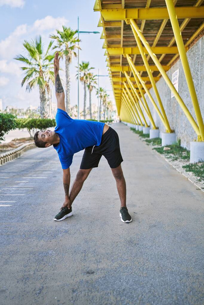 Young hispanic man stretching body muscles outdoors - 写真・画像